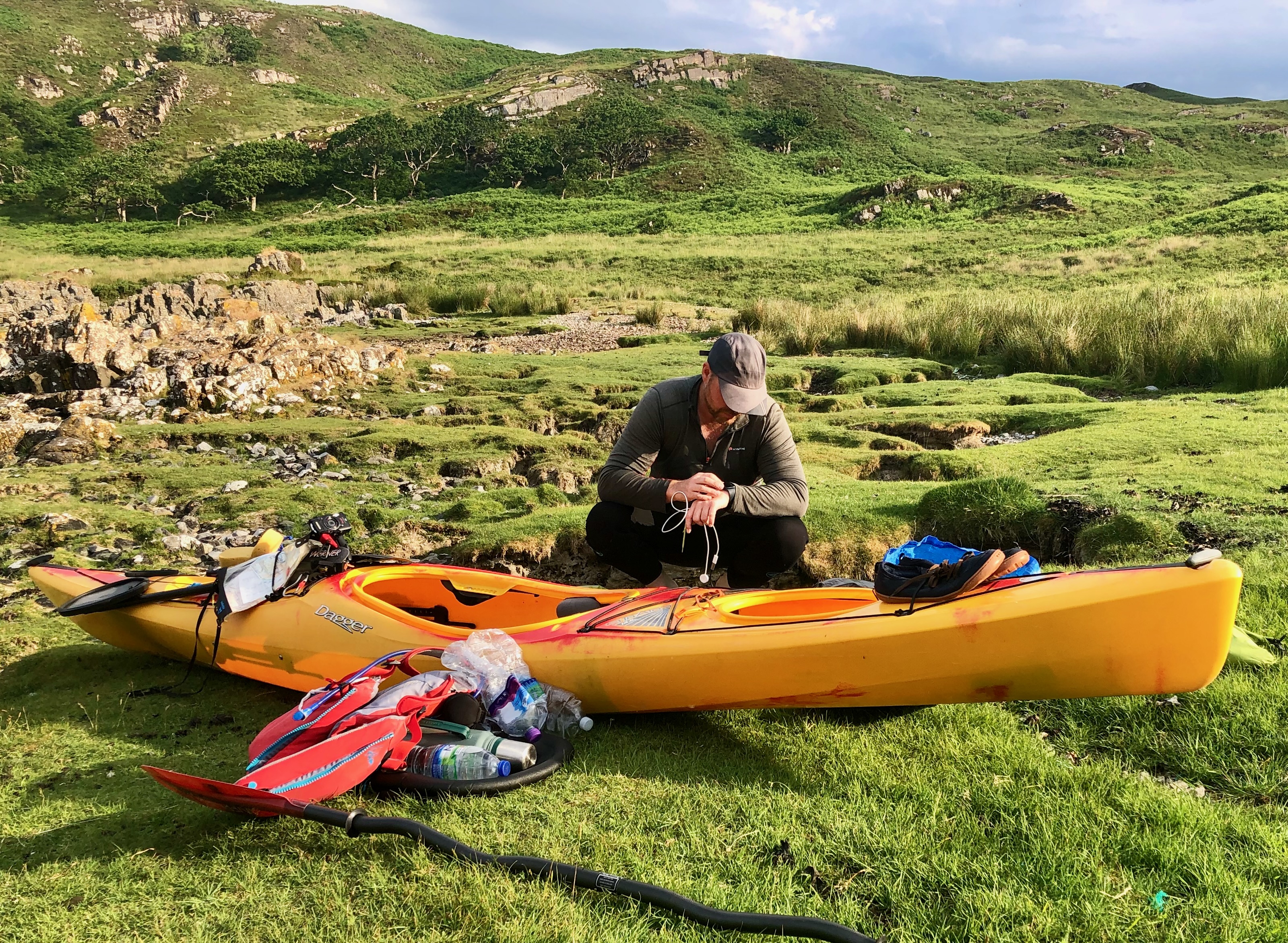 Me sat next to my yellow Dagger Stratos Kayak with various gear all around me, Apple Watch charger in hand, paddle in foreground, apple watch on my wrist, Olympus camera mounted to kayak.